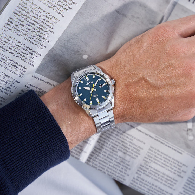 Zilverkleurige Lorus heren horloge aan een pols met een blauwe wijzerplaat.